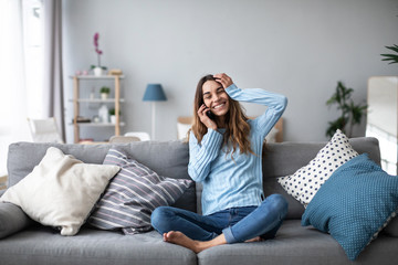 Woman emotionally talking on a mobile while sitting at home on the couch. Portrait of a positive girl.