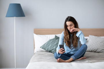 Sad woman in depression sitting at home on the couch with a mobile phone in her hands.