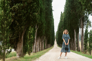 Holiday in Tuscany. Fashion portrait of young happy woman in long dress walking on pathway in typical cypresses alley in Italian countryside