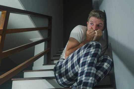 horror movie style portrait of sad and desperate man in pajamas suffering depression problem or mental disorder sitting on staircase at home hopeless crying overwhelmed