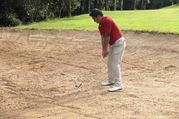 Golfer hitting the ball on the sand.