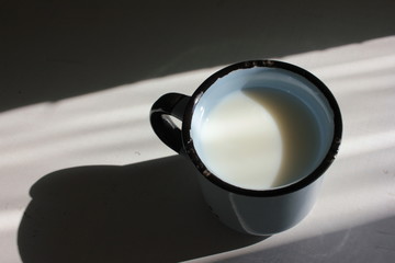 Blue ceramic cup with milk on white wooden background. Harsh daylight with deep shadows. Top view. Copy space. Healthy drink for breakfast at home