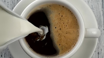 Pouring milk into coffee cup. Vintage white wooden background. Top down shot. Slow motion shot
