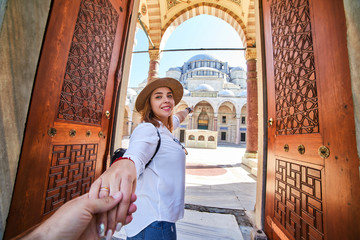 Fototapeta premium Follow me. A woman tourist in a hat leads her friend to the Turkish mosque Suleymaniye, Istanbul, Turkey. Travel and religion concept.