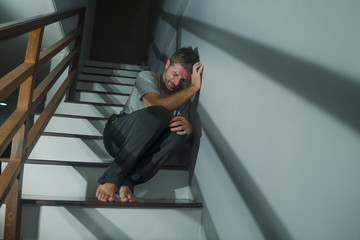 horror movie style portrait of sad and desperate man suffering depression problem or mental disorder sitting on staircase at home hopeless crying overwhelmed