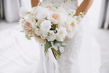 young girl in a white wedding dress holds in her hands a bouquet of flowers and greenery with a...