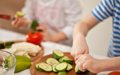 Obraz na płótnie Canvas Happy children prepares vegetables for salad in home kitchen. Healthy eating.
