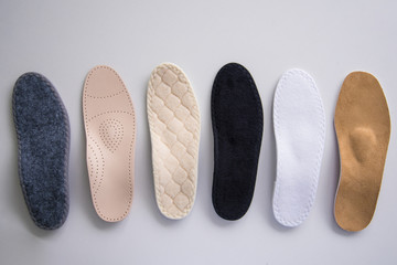 Studio photo of orthopedic insoles. A variety of orthopedic insoles are laid out in a row. Different colors and coatings: leather, cotton, microfiber. - obrazy, fototapety, plakaty