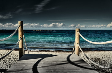 The path to a sea beach, a path consists of wooden boards, on each side a fence from a sea rope, water of azure color, clear weather