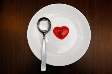 Directly above shot of silver spoon with heart shaped sauce on white plate.