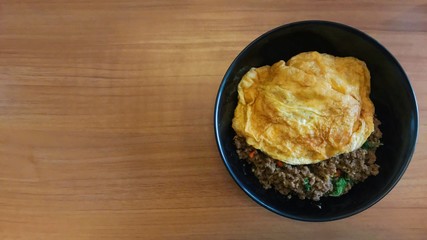 Top view popular food Stir fried pork and chilli basil with omelet on wooden table , Thai delicious yummy food. Copy space for text...