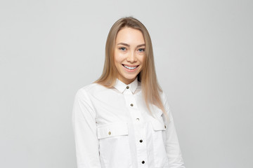 Obraz premium Beautiful young woman portrait. Portrait of a beautiful smiling blonde girl in a white shirt on a white-gray