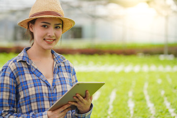Young beautiful farmer use tablet and smart device with technology to automatic control her hydroponics farm and agribusiness with happy and smile, new generation farmer