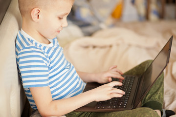 Boy kid sitting on the bed and using a digital tablet laptop notebook.