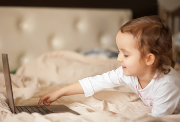 Little cute girl lying on the bed and using a digital tablet laptop notebook.