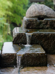 Beautiful three-tiered stone waterfall. Water flowing over rocks. Zen style garden fountain image.  Focused on foreground.