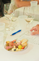 top, front view, medium distance of a round, white plate with blue rim, with food pairings of salimi, red grapes, sliced fresnch bread, sliced strawberries,  blue cheese, Prosciutto, glasses of wine