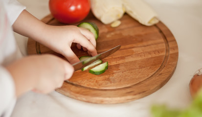 Kid child prepares vegetables for salad in home kitchen. Healthy eating.