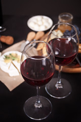 glasses of red wine and plate with assorted cheese, fruit and other snacks for party
