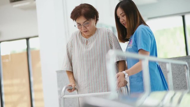 young physical therapist helping senior patient in using walker during rehabilitation