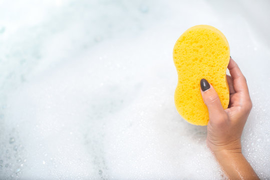 Mano de chica cogiendo una esponja de ba&ntilde;o sobre una ba&ntilde;era con espuma