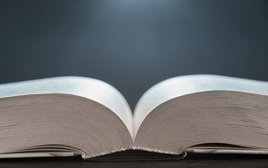 Open book illuminated by light side view close-up on a gray background. The background in blur.