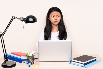 Student asian girl in a workplace with a laptop isolated on beige background with confuse face expression