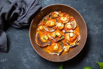 Scallops on tomato and white wine sauce with lemon, cilantro in pan on dark background. Top view