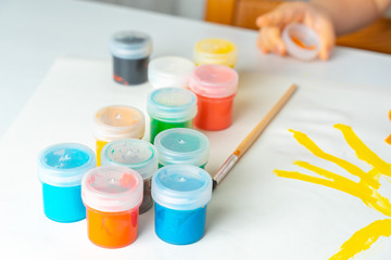 set of gouache in jars placed on a table for children's creativity. Nearby lies a brush and a sheet...