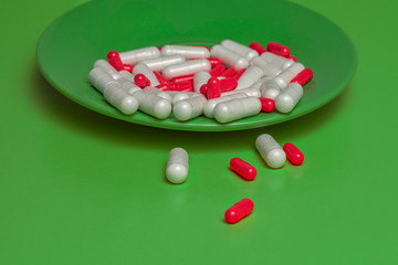 red and white pills closeup spill out of a green plate on a green background