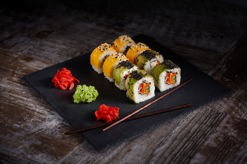 Sushi set on a square black plate of stone. Ginger and chopsticks are next to the set. Old wood background