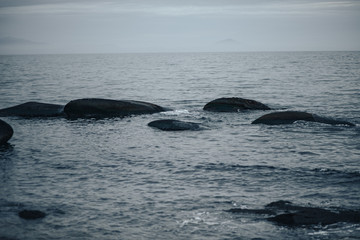 large stones sticking out of the water on the seashore, fog in the background