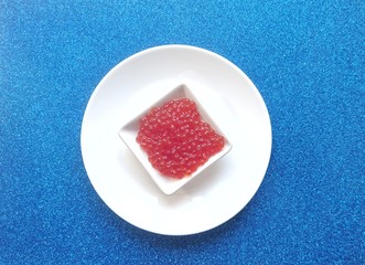 Red caviar of salmon fish in a white plate on a blue background.