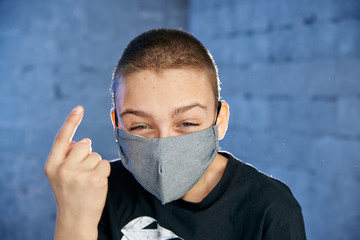 Teen boy with a protective mask against the virus on his face points a finger