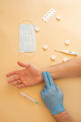 hand with antiseptic, thermometer, pills, mask on a beige background