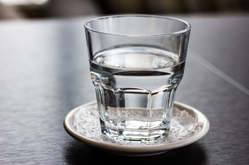 Transparent glass half filled with still water on a white saucer with a white napkin on a wooden table