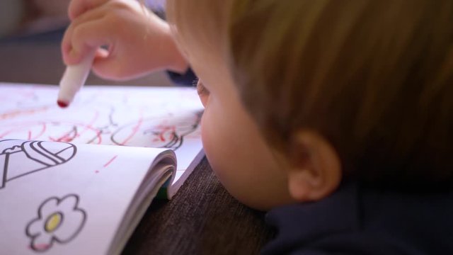 Caucasian blond boy with blue eyes, with painted face playing and painting with his markers