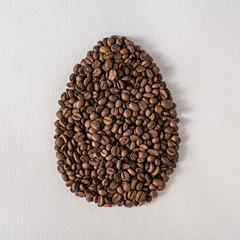 Creative flat lay composition with easter egg shape made of coffee roasted beans.Pastel colors and soft shadows. Realistic aesthetic look. Contemporary style.