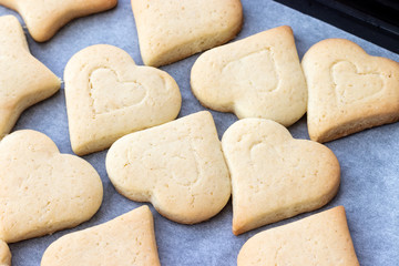 Baked shortbread cookies in the form of hearts on a baking sheet with parchment paper just taken out of the oven. Tea snack for breakfast. Selective focus. Closeup view