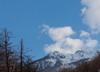 Peaks of snow-capped mountains against the blue sky with clouds