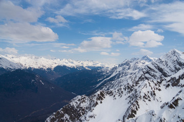 Peaks of snow-capped mountains against the blue sky with clouds