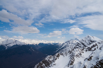Peaks of snow-capped mountains against the blue sky with clouds