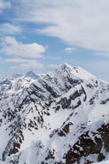Peaks of snow-capped mountains against the blue sky with clouds