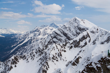 Peaks of snow-capped mountains against the blue sky with clouds