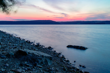 soft focus long exposure landscape photography stone coast line morning twilight lighting calm lake waters and horizon main land background view
