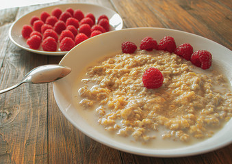 A plate of porridge and a plate of raspberries on wooden background