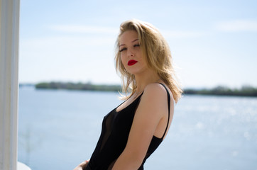 Beautiful young model. The blonde poses in nature. Red lipstick on the lips. Model in black body.