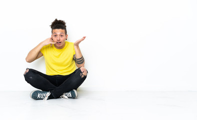 Caucasian man sitting on the floor making phone gesture and doubting