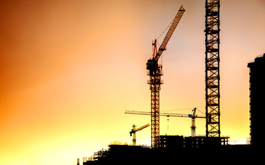 Obraz premium Silhouettes of residential buildings and construction cranes against the sunset sky.