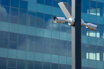 Two surveillance cameras mounted on a pillar against the background of a glass business center